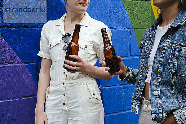 Freunde mit Bierflaschen stehen an einer bunten Wand