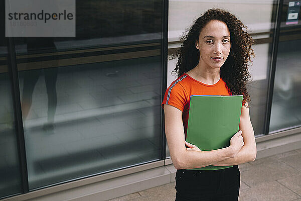 Young woman holding folder in front of glass wall