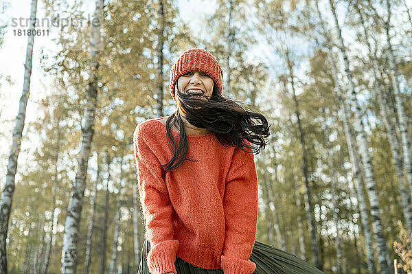 Glückliche Frau mit orangefarbenem Pullover und Strickmütze im Park