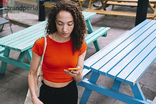 Young woman looking at mobile phone in front of picnic tables
