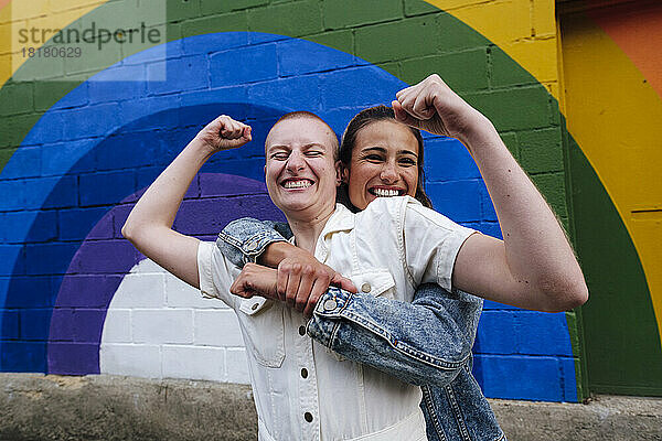 Fröhliche nicht-binäre Person mit lesbischer Frau  die Spaß vor der Regenbogenwand hat