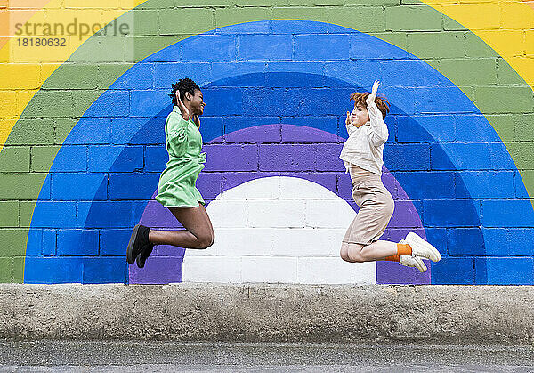 Fröhliche Freundinnen springen vor einer bunten Wand
