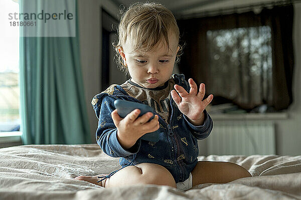 Niedlicher kleiner Junge  der im Bett auf sein Handy schaut