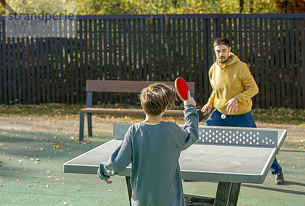 Sohn und Vater spielen an einem sonnigen Tag Tischtennis