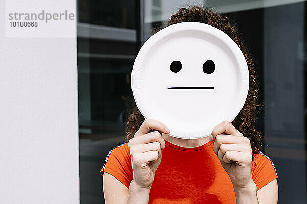 Junge Frau hält gerade Smiley-Emoticon-Platte über Gesicht