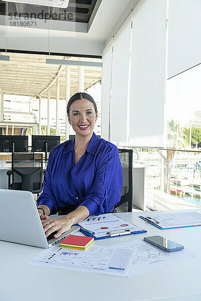 Lächelnde Geschäftsfrau mit Laptop auf dem Schreibtisch am Arbeitsplatz