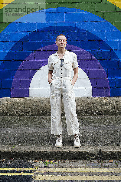 Selbstbewusste  nicht-binäre Person  die auf einem Fußweg vor einer Wand steht