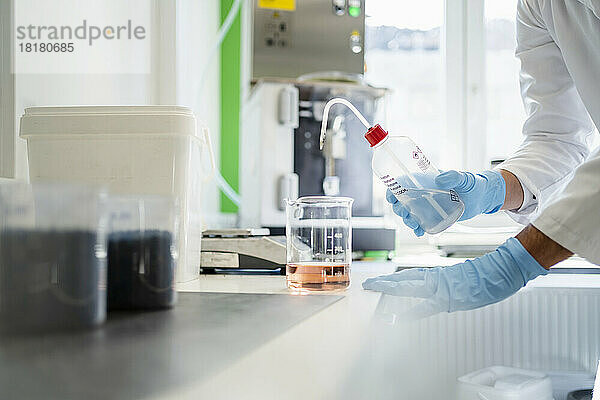 Hand eines Wissenschaftlers mit Flasche und Messbecher  der im Labor ein Thermolyseexperiment durchführt