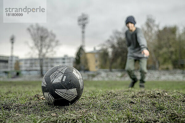 Fußball auf Gras mit Junge im Hintergrund am Sportplatz