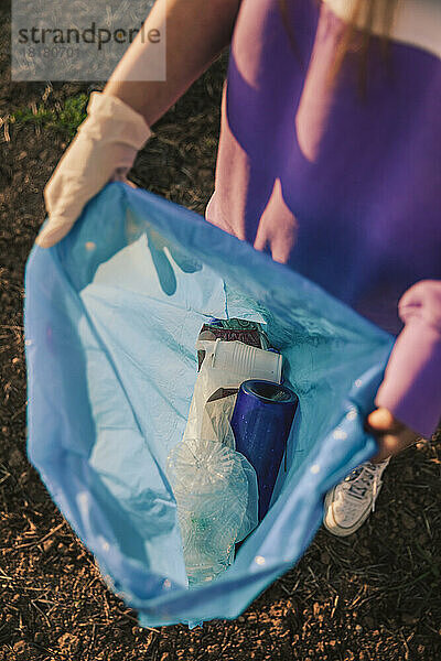 Frau zeigt Plastikflaschen im Müllsack