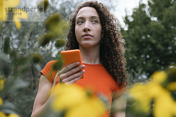 Nachdenkliche Frau steht mit Smartphone im Park