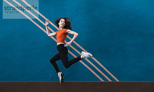 Junge Frau springt vor blaue Wand