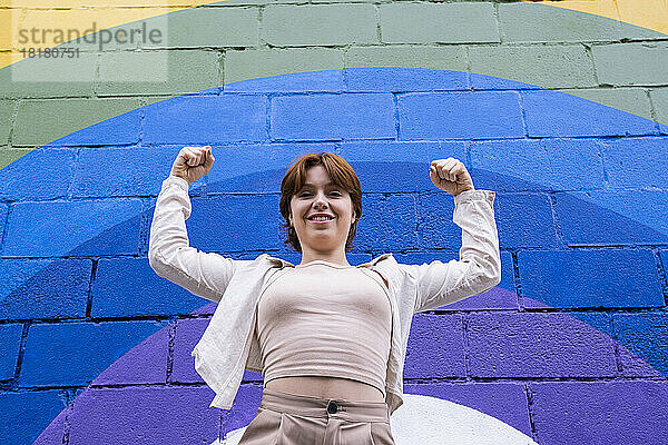 Lächelnde Frau  die vor einer bunten Wand ihre Muskeln spielen lässt