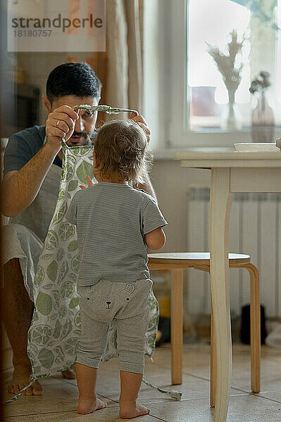 Vater trägt Schürze und kleiner Junge steht zu Hause in der Küche