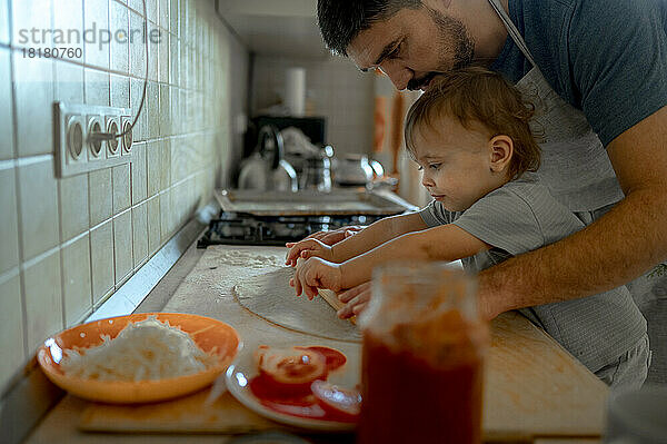 Vater und Sohn rollen gemeinsam Pizzateig in der heimischen Küche