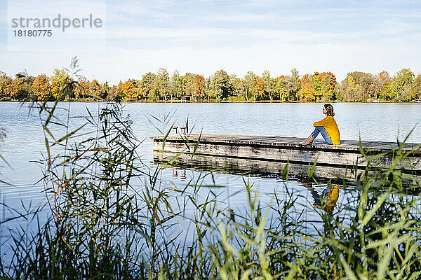 Frau sitzt auf Steg am See
