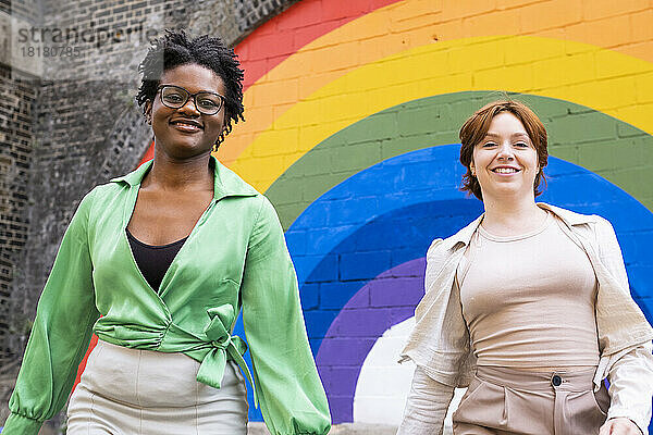 Lächelnde Frau mit Freundin vor regenbogenfarbener Wand