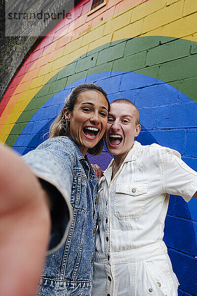 Glückliches lesbisches Paar macht ein Selfie vor einer regenbogenfarbenen Wand