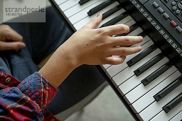 Hand of boy playing synthesizer at home