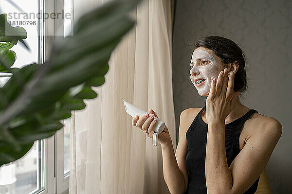 Nachdenkliche Frau  die zu Hause eine Hautpflegemaske auf das Gesicht aufträgt