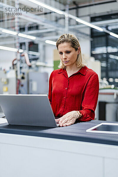 Geschäftsfrau arbeitet in der Fabrik am Laptop