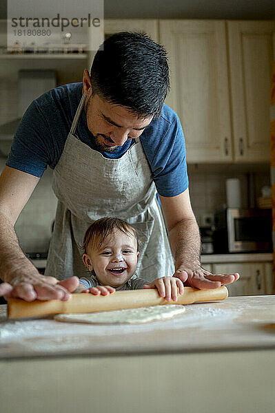 Glücklicher kleiner Junge mit Vater  der zu Hause in der Küche Pizzateig zubereitet