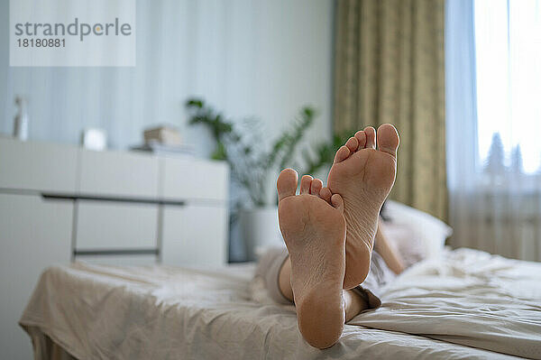 Frau mit nackten Füßen entspannt sich zu Hause im Bett