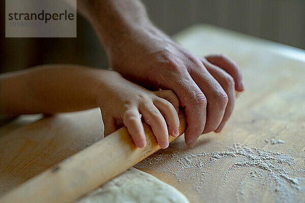 Hand eines kleinen Jungen und Vaters  der zu Hause in der Küche Pizzateig rollt