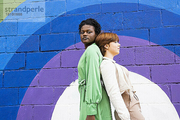 Lesbian couple standing back to back in front of colorful wall