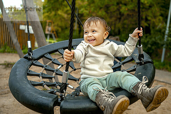 Fröhlicher süßer kleiner Junge  der im Herbstpark auf der Nestschaukel schwingt