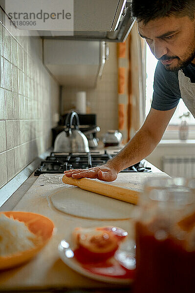 Mann rollt Pizzateig in der heimischen Küche