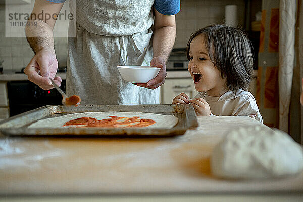 Fröhlicher Junge mit Vater  der zu Hause Pizza zubereitet