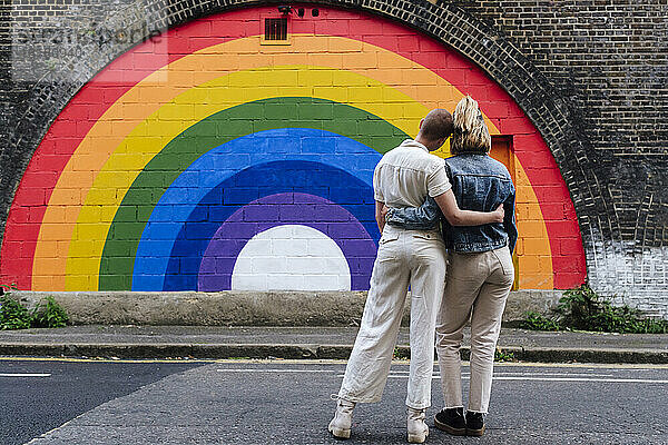 Schwules Paar steht zusammen vor einer regenbogenfarbenen Wand