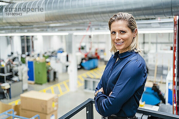 Selbstbewusste Geschäftsfrau im blauen Hemd steht mit verschränkten Armen in der Fabrik