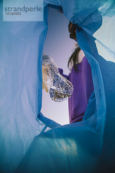 Junge Frau sammelt Plastikflasche im Müllsack