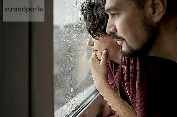 Vater und Sohn schauen zu Hause durch das Fenster