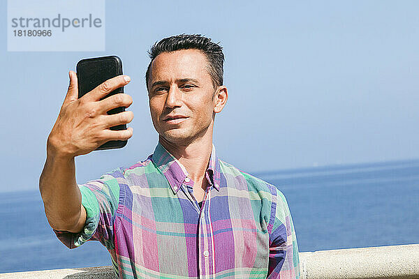 Lächelnder Mann macht ein Selfie mit dem Smartphone vor dem Meer