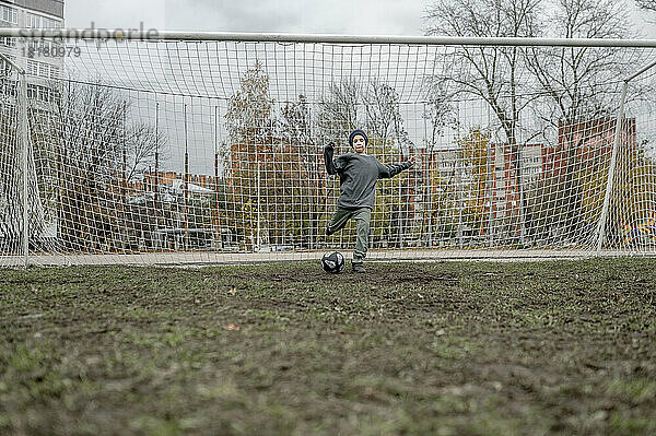 Junge kickt Ball vor Torpfosten auf Sportplatz