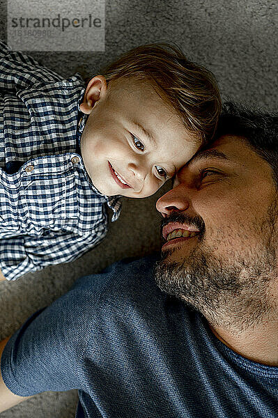 Happy father lying by son on carpet at home