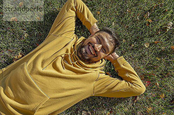 Fröhlicher Mann in gelber Kapuzenjacke liegt auf Gras im Park