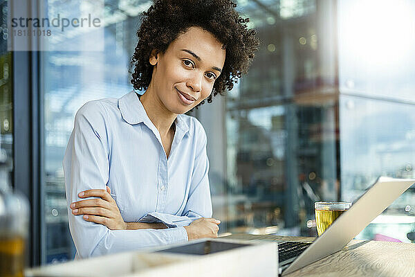 Lächelnde Geschäftsfrau mit verschränkten Armen und Laptop im Büro
