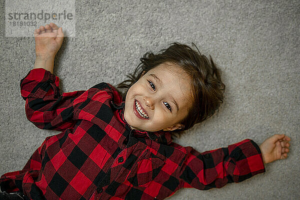 Cute happy boy in plaid shirt lying on carpet
