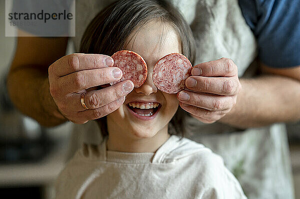 Vater bedeckt die Augen seines Sohnes mit Peperoni in der heimischen Küche