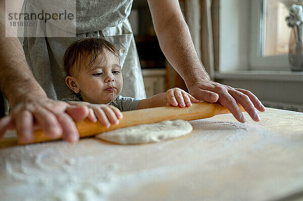 Mann mit Baby rollt zu Hause in der Küche Pizzateig