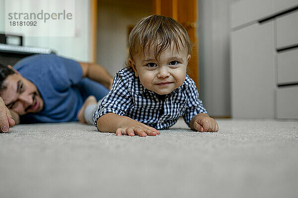 Lächelnder Sohn und Vater liegen zu Hause auf dem Teppich