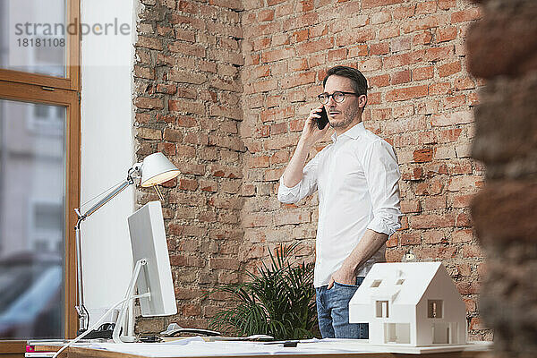 Reifer Geschäftsmann mit der Hand in der Tasche  der im Büro auf dem Smartphone spricht