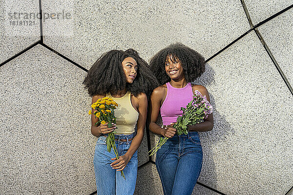 Glückliche junge Frau mit einer Freundin  die Blumen an der Wand hält