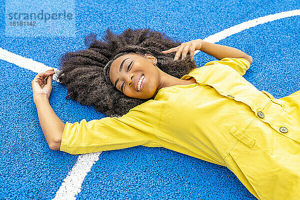 Glückliche Frau mit Afro-Frisur liegt auf blauem Basketballplatz