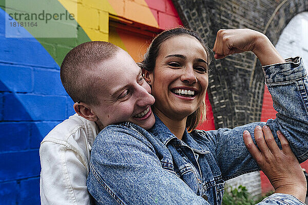 Glückliche lesbische Frau zeigt Bizeps vor der Regenbogenwand