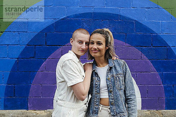 Lesbisches Paar steht zusammen vor einer bunten Wand